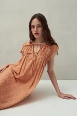 Vestido largo color salmón con estampado abstracto, escote con lazo y mangas cortas. Diseño fluido con frunces en el pecho.