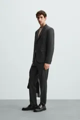 Pantalón de vestir gris oscuro, corte slim fit, con bolsillos laterales y traseros de ojal. Cierre frontal con cremallera y botón.