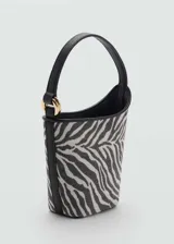 Bolso tipo bucket con estampado de cebra en blanco y negro, asa corta rígida, cierre magnético y forro interior.