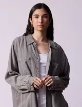 Camisa de jean celeste, marca Hester & Orchand, de corte oversize con cuello con solapa, escote en V y abertura central con botones. Delantera con bolsillos aplicados, mangas largas regulables con presilla y botón, y ruedo desflecado.