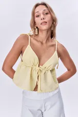 Top amarillo pálido con escote en V, breteles finos con lazos en los hombros y corte holgado con frunce y lazo ajustable en el centro del busto.