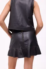 Falda corta negra de efecto cuero, estilo wrap o cruzada, con ajuste lateral mediante lazos de cuero y terminación con volante o ruedo con volado. Presenta costuras contrastantes en color claro.
