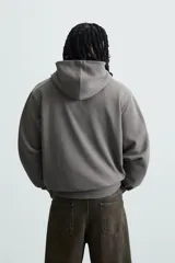 Sudadera con capucha color crudo, de corte relajado, confeccionada en tejido de algodón con interior rizado. Cuenta con cuello con capucha, manga larga, bolsillo frontal tipo canguro y acabados en rib.