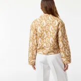 Chaqueta corta acolchada color beige con estampado abstracto en blanco, cuello redondo y cierre frontal con botones.