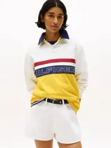 Chomba de rugby Tommy Hilfiger Sailing, unisex, de corte amplio y hombros caídos. Diseño color block blanco, amarillo y azul, con logo de la marca bordado en el pecho.