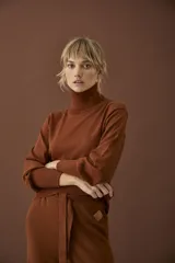 Polera color ladrillo, entallada, de tejido de punto fino, con cuello alto, mangas largas abullonadas y puños acanalados.