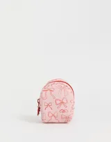 Llavero con forma de mochila pequeña color rosa claro con estampado de moños rojos y cierre con cremallera roja.