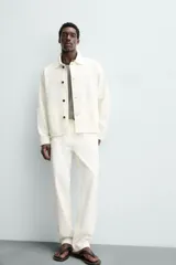 Pantalón de jean color blanco, corte recto, con bolsillos frontales y traseros, y cierre frontal con cremallera y botón.