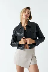 Sobrecamisa cropped de cuero sintético color negro, con cuello clásico, cierre frontal con botones, mangas largas y bolsillos frontales con solapa.