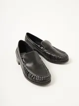 Mocasines de cuero negro con apliques de charol y pespuntes blancos.