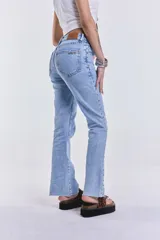 Jean de denim celeste, de corte recto y tiro medio, sin lycra. Presenta tachas metálicas en los laterales.