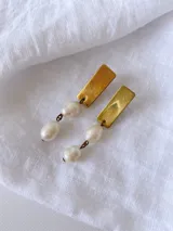 Aros colgantes con base rectangular dorada y dos perlas blancas unidas por aros de metal.