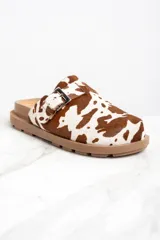 Zuecos con capellada de cuero con estampado animal print de vaca, base marrón con suela track y hebilla metálica ajustable.