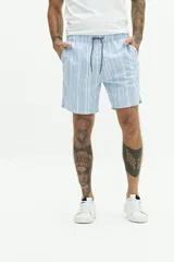 Short de baño largo azul con estampado abstracto de hojas en tonos azules más claros. Posee cintura elástica con cordón de ajuste gris, bolsillos laterales y un bolsillo trasero.