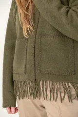 Chaqueta corta color gris oscuro confeccionada en lana merino hervida, con cuello redondo, mangas largas y bolsillos frontales. Presenta detalle de flecos en el ruedo.
