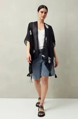 Poncho de gasa liviana color negro, con mangas amplias estilo kimono y bordados florales blancos. Presenta borlas decorativas en los bordes.