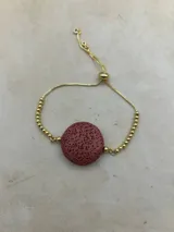 Pulsera dorada con tres piedras volcánicas negras y cierre corredizo.