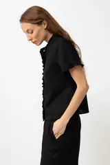 Camisa negra de lino con cuello mao y volados en cuello y mangas cortas.