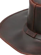 Sombrero de cuero marrón oscuro, estilo vaquero o fedora de ala ancha, con corona moldeada y orificios de ventilación laterales.