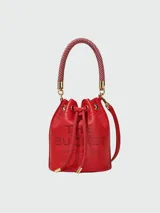 Bolso tipo bucket de cuero color rojo con logo de la marca grabado en el frente. Tiene asa corta de cuerda trenzada y correa larga de cuero ajustable y removible.