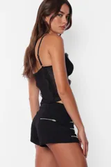 Microshort negro de gabardina elastizada con cierre metálico a la vista en la cartera y bolsillos traseros. En los laterales delanteros presenta cierres metálicos decorativos.
