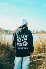 Canguro negro con capucha y cordones ajustables. Estampado en la espalda con la frase "Glassy Waves", una flor y "Good Vibes".