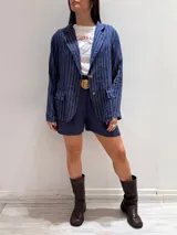 Blazer azul marino con rayas verticales blancas, confeccionado en lino italiano. Tiene botones de coco, solapas clásicas y bolsillos delanteros.