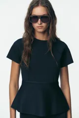 Top azul marino de punto con cuello redondo y manga corta. Tiene corte a la cintura y peplum en el bajo.