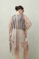 Poncho color beige de tejido calado con flecos en el ruedo.