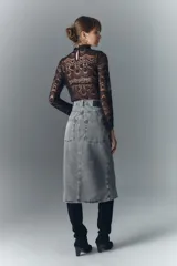 Falda midi de denim rígido, color gris claro lavado, con botones metálicos grabados en el frente y recortes verticales.