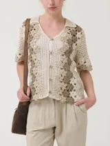 Sweater tejido a crochet color crema con flores bordadas en tonos beige y marrón. Tiene cuello camisero, mangas cortas y cierre frontal con botones.