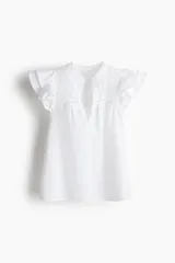 Blusa blanca de algodón con corte holgado, cuello mao y mangas cortas con volados. Presenta broderie en el canesú delantero.
