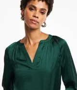 Blusa verde esmeralda de tela satinada, con escote en V, mangas largas con puños abotonados y espalda fruncida.
