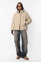 Campera puffer beige de corte oversize, confeccionada en textil impermeable. Cuenta con capucha forrada con tancas y elástico, cuello alto, cierre frontal con cartera y abrojo, bolsillos ribete con cierre, mangas desmontables con mitones y cintura ajustable con elástico y tancas. Incluye cinta gross estampada para transportarla al hombro y bolsillo interno con cierre invisible.