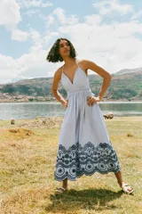 Vestido midi a rayas verticales azules y blancas, con escote en V, tirantes finos y cintura elástica. Presenta bordados florales calados en el ruedo.