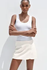 Falda pantalón corta color blanco, de tiro medio con abertura en el delantero y cierre lateral con cremallera.