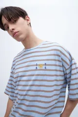 Remera verde con rayas horizontales azul marino, corte boxy y estampado con el número 1956 en el pecho.