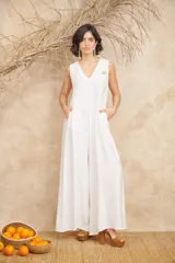 Mono blanco de corte amplio con escote en V, sin mangas y prendedor dorado en el pecho. Incluye bolsillos laterales.