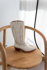 Bota de caña media color marrón con bordados decorativos en hilo color crema, puntera en punta y taco de madera.