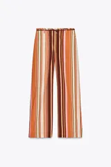 Pantalón de tiro medio con estampado de rayas verticales en tonos marrón, naranja, rosa y beige. Cuenta con trabillas en la cintura, cinturón ajustable con lazadas, bolsillos laterales y cierre frontal con cremallera y botones.