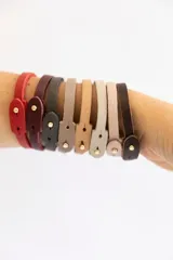 Set de cuatro pulseras finas de cuero en colores borgoña, rosa pálido, gris y verde oscuro. Cada pulsera tiene un cierre con botón metálico y algunas tienen palabras grabadas.