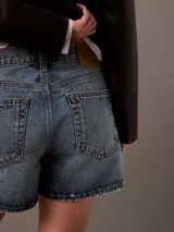 Shorts de jean de tiro medio con lavado azul claro vintage, corte holgado de los 90, bajo desflecado, cierre de botón con cremallera y diseño de cinco bolsillos.