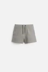 Short de baño con textura seersucker a rayas verticales azul marino y blanco. Tiene cintura elástica ajustable con cordón, bolsillos frontales y traseros, aberturas laterales en el bajo y forro interior.