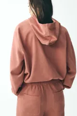 Chaqueta corta color rosa con capucha y manga larga terminada en puño. Tiene bolsillos de vivo en el delantero, bajo ajustable con cordones elásticos y cierre frontal con cremallera.