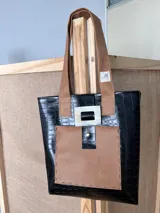 Bolso tote negro con textura símil cuero de cocodrilo, con bolsillo frontal marrón y herrajes plateados.