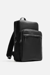Mochila marrón de cuero sintético con textura grabada. Tiene un compartimento principal con cierre de cremallera, un bolsillo interno para dispositivos electrónicos de hasta 13 pulgadas y un bolsillo interno con cremallera. En la parte delantera tiene un bolsillo con cremallera. La parte posterior es acolchada y tiene una banda de sujeción para equipaje. Tiene un asa de mano y dos asas de hombro ajustables y acolchadas.