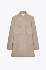 Abrigo color beige confeccionado en lana. Tiene cuello subido, mangas largas con hombreras, forro interior combinado y cierre frontal cruzado con botones metálicos.