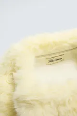 Bolso de mano tipo sobre, color negro, con textura de pelo sintético. Forro interior satinado con bolsillo con cremallera. Cierre con clip y detalle de arandela lateral.