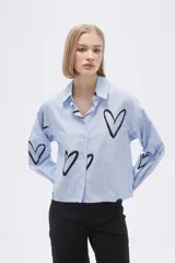 Camisa celeste a rayas verticales blancas, con cuello clásico, cierre frontal con botones y estampado de corazones negros.