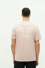 Remera verde de manga corta con cuello redondo y estampado en la espalda con la frase "Côte d'Azur Surfer avec les mouettes" y un dibujo de una sombrilla, una reposera y gaviotas.
